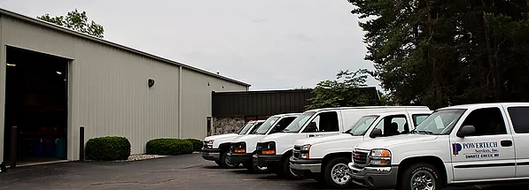 Five white utility vans parked outside warehouse